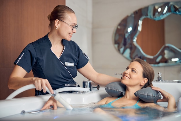 Jeune femme thérapeute souriant à son patient pendant la procédure d'hydrothérapie dans un salon de spa