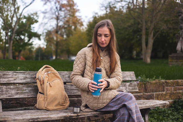 Jeune femme avec un thermos est assis sur un banc de parc