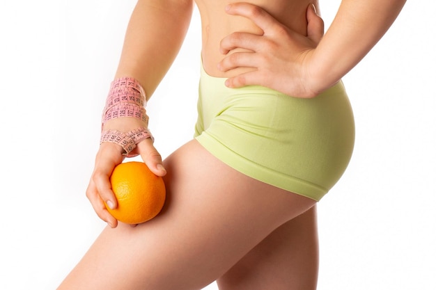 Une jeune femme tient un agrume orange sur fond blanc Le concept de problème de cellulite