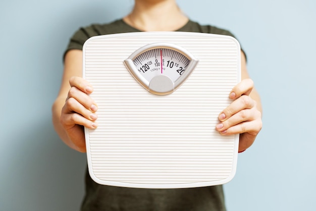 Une jeune femme tient une balance blanche pour vérifier les résultats de son régime alimentaire