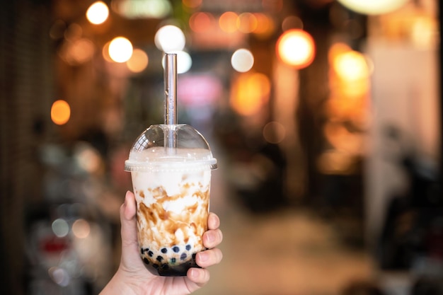 Jeune femme tient à boire du thé au lait à bulles de tapioca parfumé au sucre brun avec de la paille en verre au marché de nuit de Taiwan close up bokeh