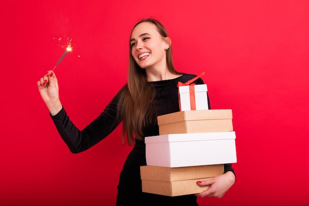 Une jeune femme tient des cadeaux de Noël et des cierges magiques sur fond rouge