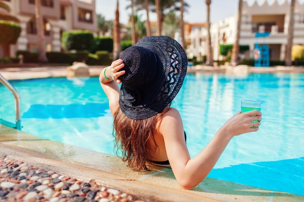 Jeune femme tient un cocktail dans la piscine de l'hôtel Vacances d'été Tout compris