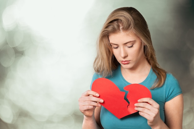 Jeune femme tient un cœur brisé isolé sur fond.