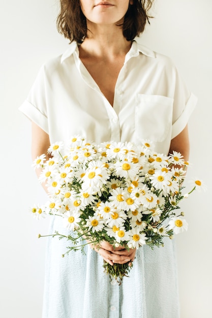 Jeune femme tient dans les mains bouquet de fleurs de marguerite blanche sur une surface blanche