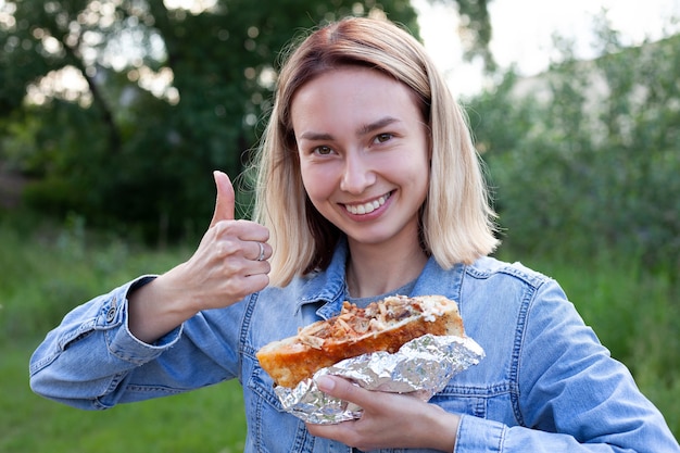 Photo une jeune femme tient un gros hamburger la femme sourit et montre son pouce vers le haut nourriture malsaine nourriture lourde