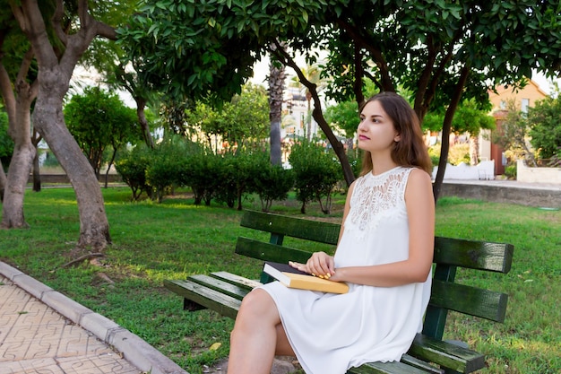 Jeune femme tient un livre et rêve de quelque chose à l'extérieur