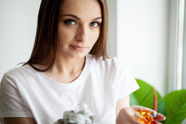 Une jeune femme tient de nombreuses pilules avec des compléments alimentaires dans ses mains