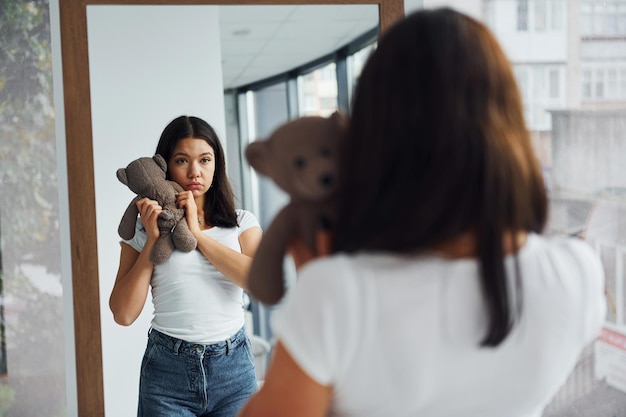 Une jeune femme tient un ours en peluche et se regarde dans le miroir