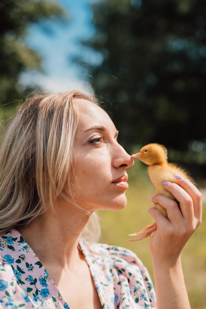 Une jeune femme tient un petit caneton dans sa main touchant son bec avec son nez