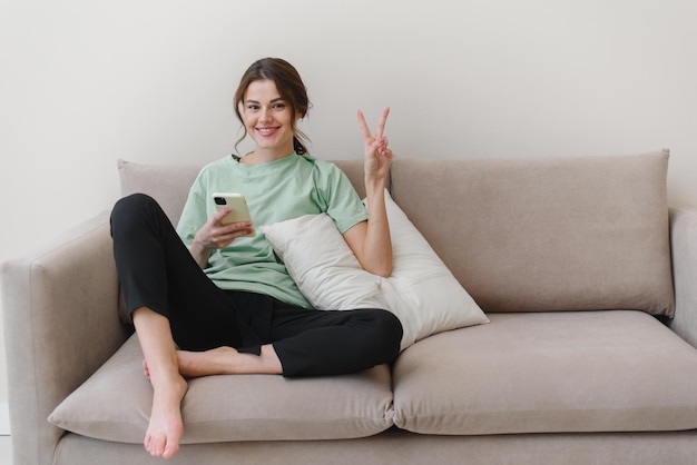 Une jeune femme tient un téléphone montrant un geste tendance et regarde la caméra