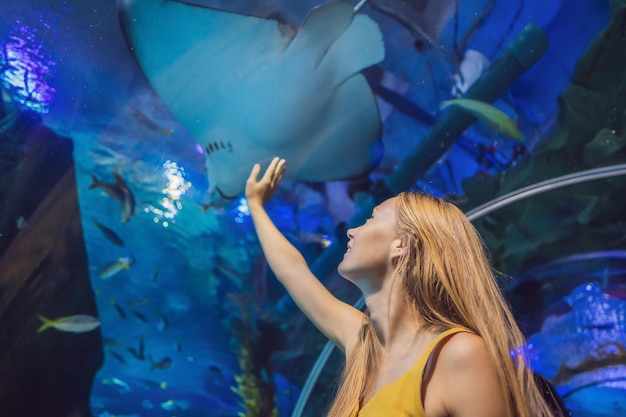 Jeune femme touche un poisson raie dans un tunnel de l'océanarium