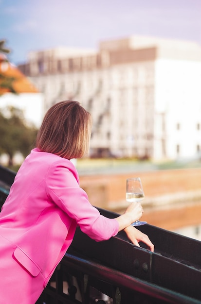 Jeune femme touriste debout avec un verre de vin blanc au pont dans la rivière de la ville européenne à l'arrière-plan