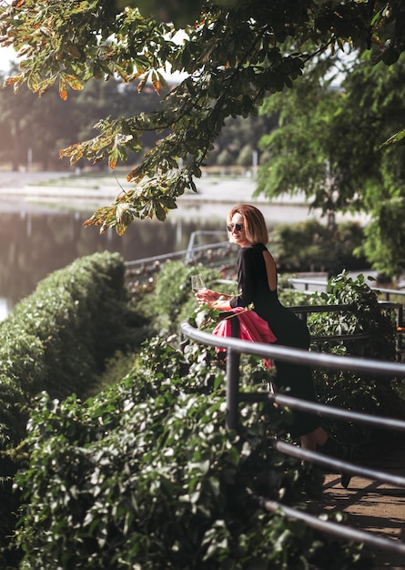 Jeune femme touriste debout avec un verre de vin blanc au pont dans la rivière de la ville européenne à l'arrière-plan