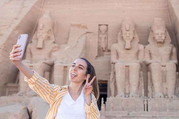 Jeune femme touriste prenant un selfie avec tounge out et signe de paix dans le temple d'Abou Simbel en Égypte