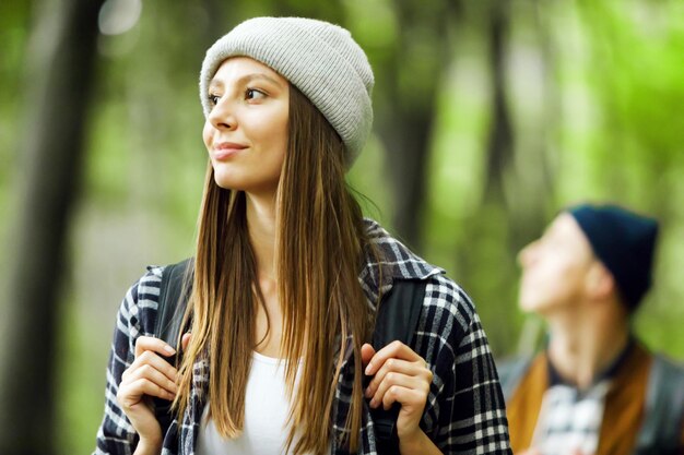 Jeune femme touristique aux cheveux longs avec sac à dos marchant dans la forêt avec son amie en arrière-plan