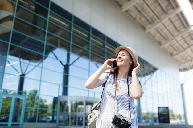 Jeune femme touristique joyeuse voyageur avec un appareil photo rétro vintage parle sur un ami d'appel de téléphone portable