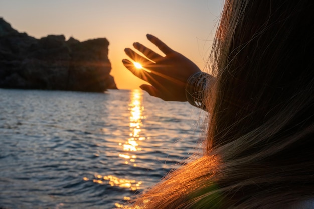 Une jeune femme touristique tenant une tasse de café tout en étant assis à l'extérieur et profitant du lever du soleil sur le paysage de montagne de la mer