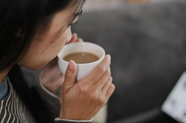 Photo une jeune femme en train de boire sa tasse de thé ou de café assise sur le canapé.