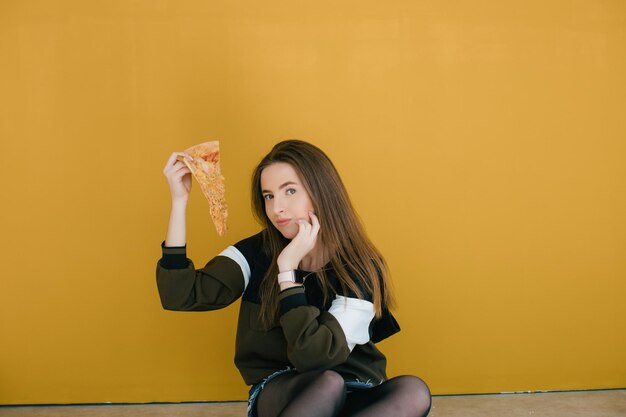 Jeune femme avec une tranche de délicieuse pizza sur un fond de couleur