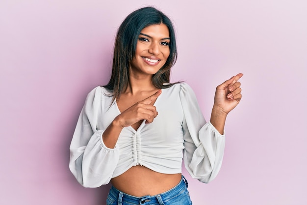 Jeune femme transgenre transsexuelle latine portant des vêtements décontractés souriant et regardant la caméra pointant avec les deux mains et les doigts sur le côté