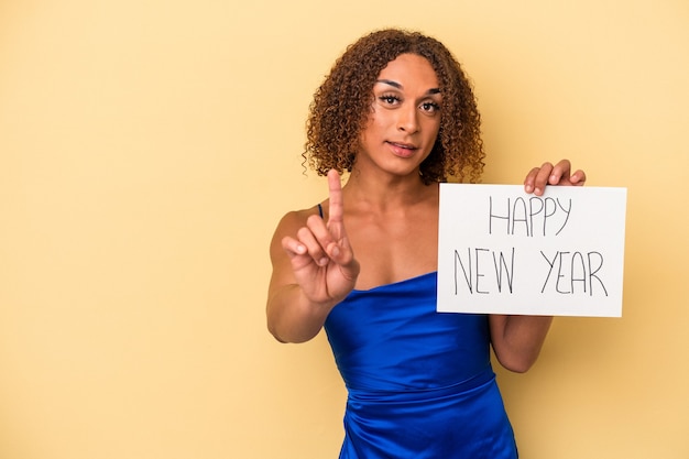 Jeune femme transsexuelle latine célébrant le nouvel an isolé sur fond jaune montrant le numéro un avec le doigt.