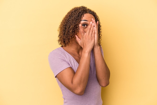 Jeune femme transsexuelle latine isolée sur fond jaune clignote à travers les doigts effrayée et nerveuse.