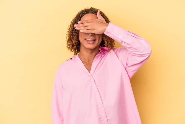 Photo jeune femme transsexuelle latine isolée sur fond jaune couvre les yeux avec les mains, sourit largement en attendant une surprise.