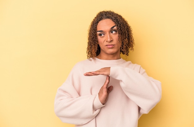 Jeune femme transsexuelle latine isolée sur fond jaune montrant un geste de temporisation.