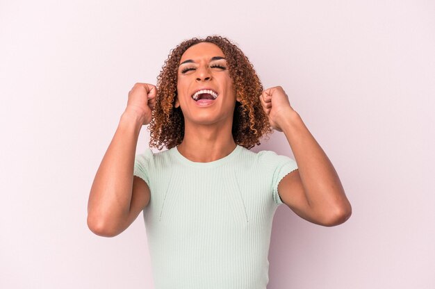 Jeune femme transsexuelle latine isolée sur fond rose célébrant une victoire, passion et enthousiasme, expression heureuse.