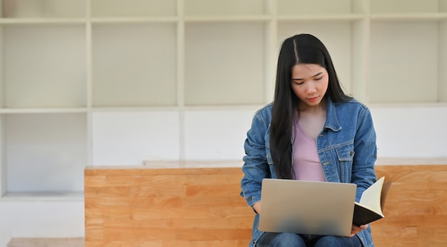 Jeune femme travaillant dans la bibliothèque avec du papier pour ordinateur portable et ordinateur portable.