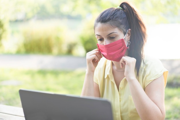 Jeune femme travaillant à l'extérieur avec un ordinateur portable et portant un masque facial rouge pendant la période du coronavirus Femme utilisant un masque protecteur pour prévenir la propagation du covid19 Nouveau concept normal et travail intelligent