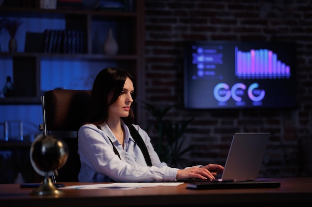 Jeune femme travaillant avec un ordinateur portable au bureau Employé de bureau analysant des graphiques et des graphiques surchargés tout en étant assis au bureau jusqu'à la fin