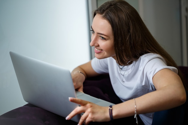 Jeune femme travaillant sur un ordinateur portable. Jolie fille utilisant un ordinateur portable, travaillant à la maison, se relaxant sur le canapé. Télétravail, télétravail, quarantaine, nomade numérique, concept rester à la maison