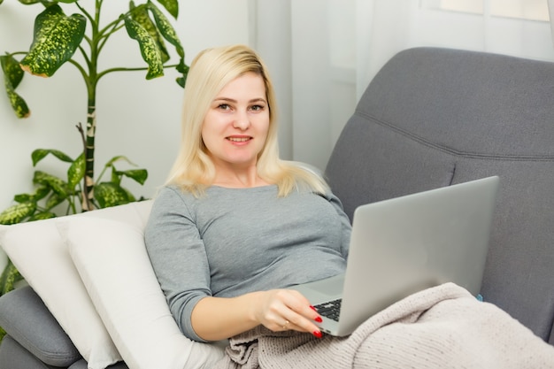 Jeune femme travaillant sur un ordinateur portable à la maison. Fille assise sur un lit avec un ordinateur. Quarantaine, restez à la maison concept. Coronavirus (COVID-19