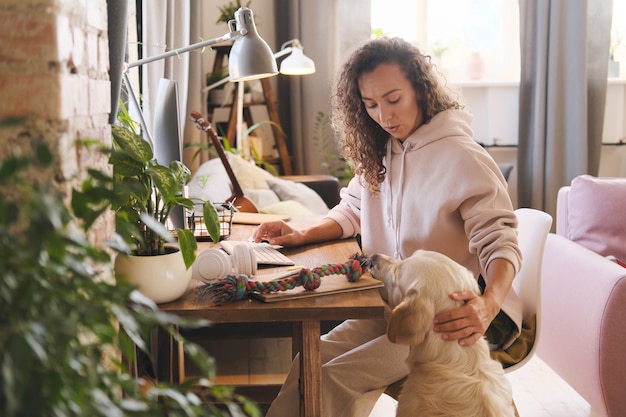 Jeune femme travaillant à la table avec ordinateur à la maison tout en chien voulant jouer avec elle