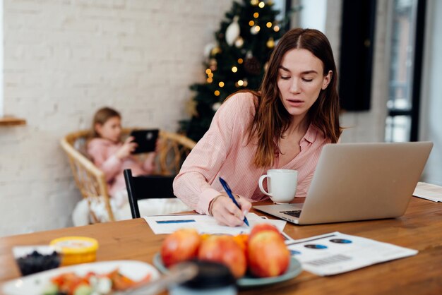 Une jeune femme travaille à la maison pendant que sa fille reste à la maison pendant les vacances d'hiver