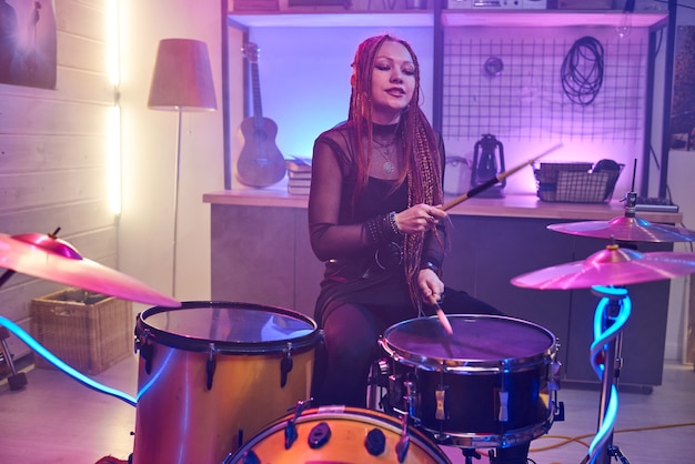 Jeune femme avec des tresses frappant des cymbales de batterie pendant la répétition