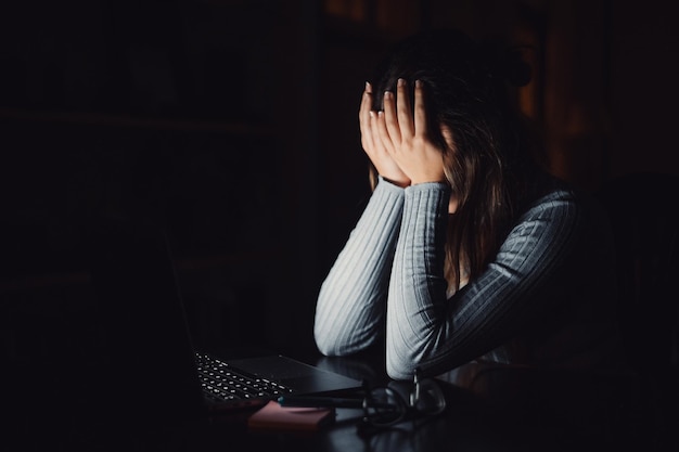 Une jeune femme triste et fatiguée se sentant mal en se couvrant le visage avec les mains tout en travaillant à la maison à l'intérieur Femme épuisée et stressée à étudier la nuit