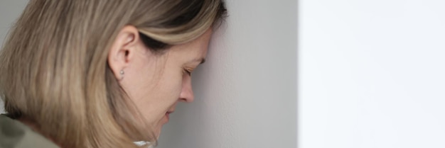 Une jeune femme triste s'appuie contre le mur blanc concept de gros plan épuisement émotionnel douleur mentale