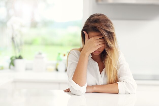 Jeune femme triste souffrant de maux de tête dans la cuisine