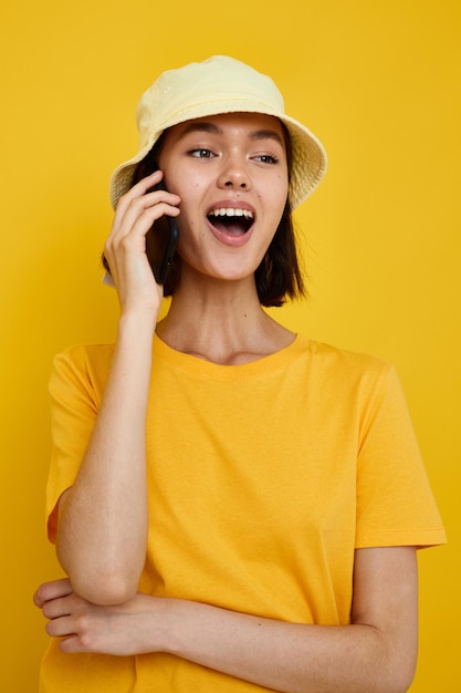 Jeune femme tshirt jaune et chapeau style été avec téléphone fond jaune