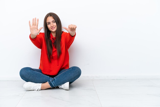 Jeune femme ukrainienne assise sur le sol isolé sur fond blanc comptant six avec les doigts