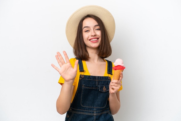 Jeune femme ukrainienne avec une glace au cornet isolée sur fond blanc saluant avec la main avec une expression heureuse