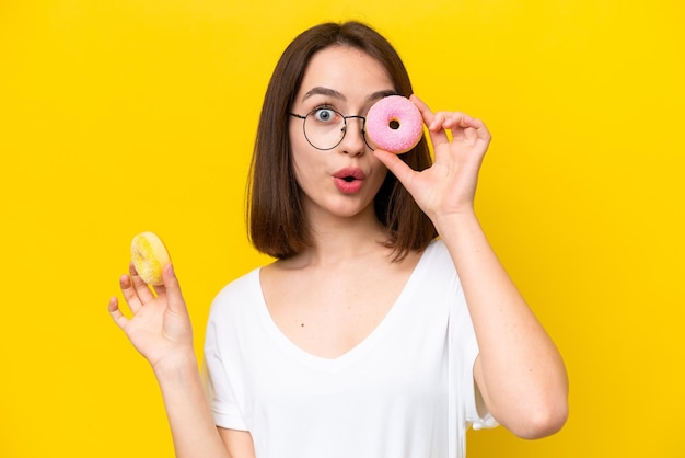 Jeune femme ukrainienne isolée sur fond jaune tenant un beignet dans un œil