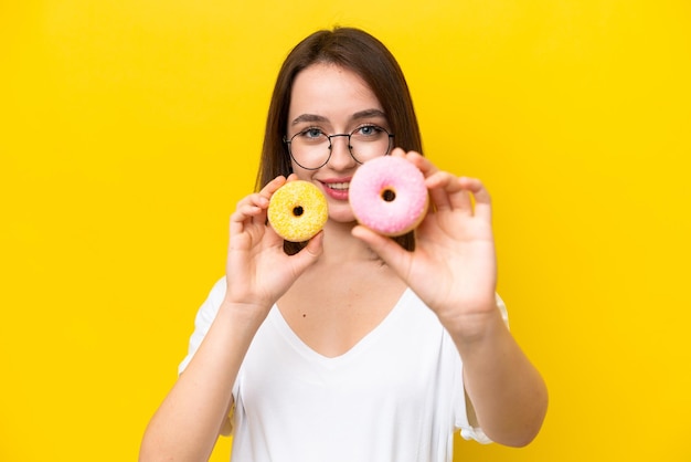 Jeune femme ukrainienne isolée sur fond jaune tenant des beignets avec une expression heureuse