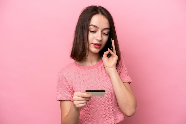 Jeune femme ukrainienne isolée sur fond rose achetant avec le mobile avec une carte de crédit