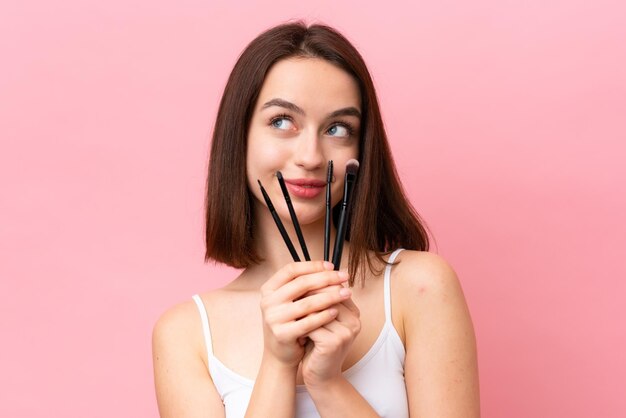 Jeune femme ukrainienne isolée sur fond rose tenant un pinceau de maquillage et levant les yeux