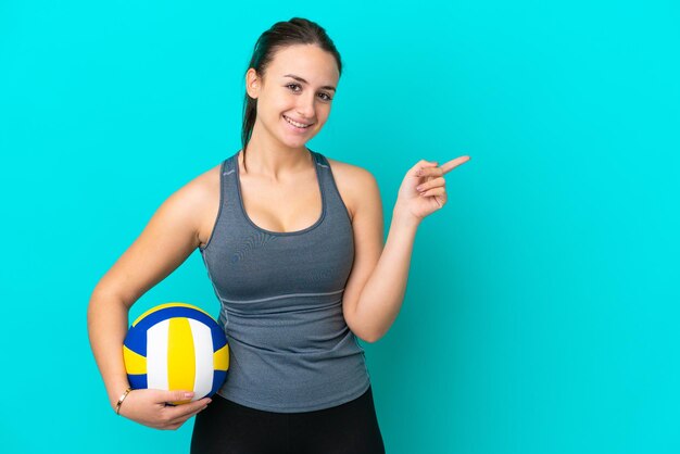 Jeune femme ukrainienne jouant au volley-ball isolé sur fond bleu pointant le doigt sur le côté