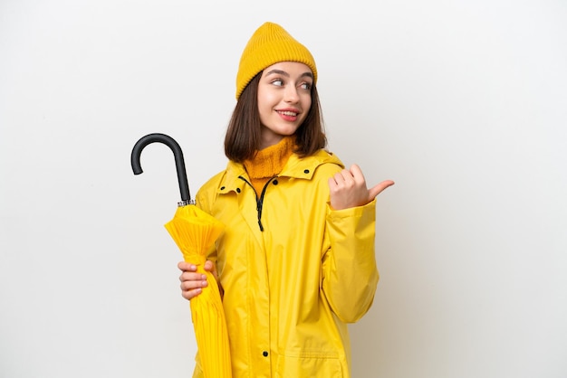 Jeune femme ukrainienne avec manteau imperméable et parapluie isolé sur fond blanc pointant vers le côté pour présenter un produit